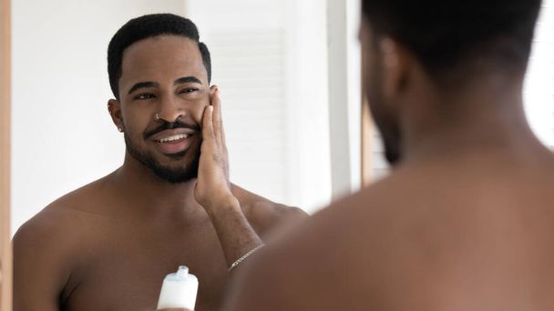 Young african american man apply facial cream in bathroom - Фото, зображення