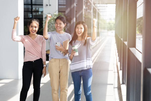 Group Cheerful young Asian woman three people raised fist celebration is happy after receive good news or work successfully in modern office. success and winning concept - Photo, Image