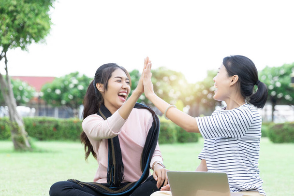 Boldog fiatal ázsiai nő ad pacsit kollégáinak, miután jó híreket kapott a laptopjáról. A nők izgatottak a sikeres közös munka miatt. siker és győzelem - Fotó, kép