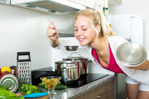 Positive young girl preparing soup in cooking pot on kitchen at home - Φωτογραφία, εικόνα