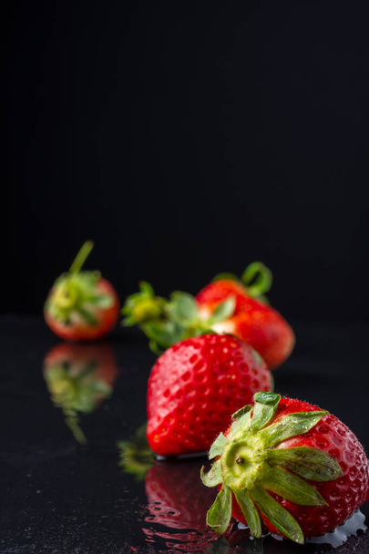 Nahaufnahme von Erdbeeren auf nassem schwarzen Schieferstein und Reflexion, mit selektivem Fokus, schwarzer Hintergrund, vertikal, mit Kopierraum - Foto, Bild