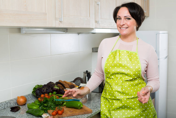 Happy female in apron preparing dinner with fresh veggies indoor - Foto, Bild