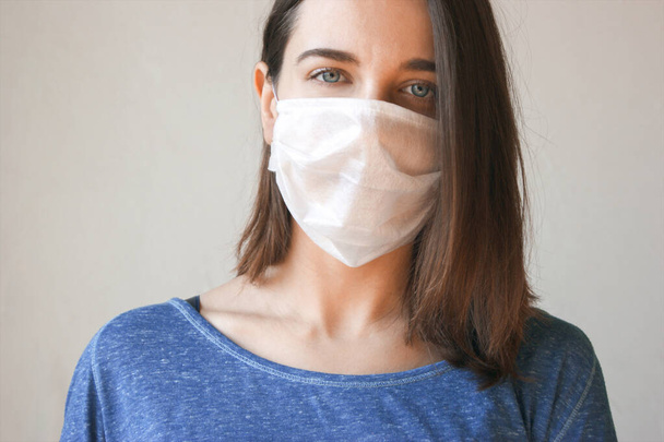 Το πρόσωπο μιας νεαρής γυναίκας που φοράει ιατρική μάσκα για την πρόληψη μικροβίων, τοξικών αναθυμιάσεων και σκόνης. Πρόληψη βακτηριακής λοίμωξης από τον ιό Corona ή το Covid 19. - Φωτογραφία, εικόνα