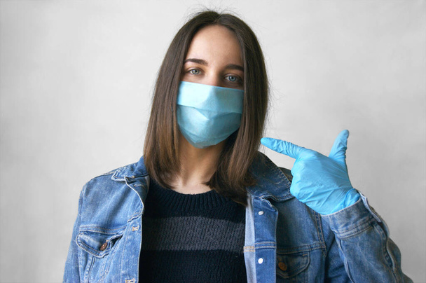 Auf dem Bild einer jungen Frau mit medizinischer Maske und Handschuhen zeigt sie mit dem Zeigefinger auf einer Maske, die alle auffordert, während einer Pandemie und Quarantäne zu Hause zu bleiben. Prävention bakterieller Infektionen mit Coronavirus oder Covid 19. - Foto, Bild