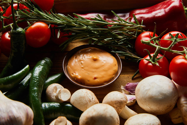 köstliche Sauce in Schüssel in der Nähe von frischem reifem Gemüse, Rosmarin und Pilzen - Foto, Bild