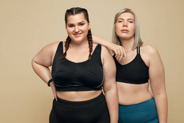 Body Positive. Plus Size Models Portrait. Fat Women In Sportswear On Beige Background. Fitness For Active Lifestyle. - Foto, imagen
