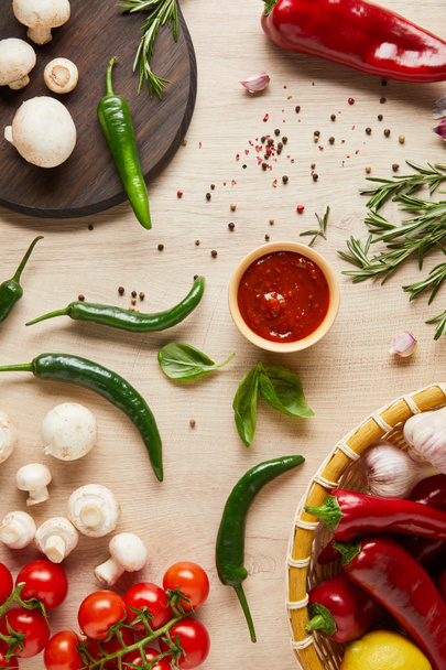 Tahta masadaki taze sebzelerin, otların, baharatların ve mantarların yanında kasedeki leziz domates sosunun üst görüntüsü. - Fotoğraf, Görsel