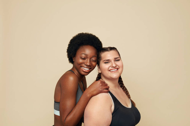 Fitness. Caucasian And African Women Portrait. Different Race Models In Fitness Clothes Posing On Beige Background. Body Positive As Lifestyle.  - Foto, imagen