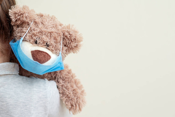 Ours en peluche avec masque médical protecteur sur l'épaule de l'enfant. Soins de santé et concept de protection contre les virus
. - Photo, image