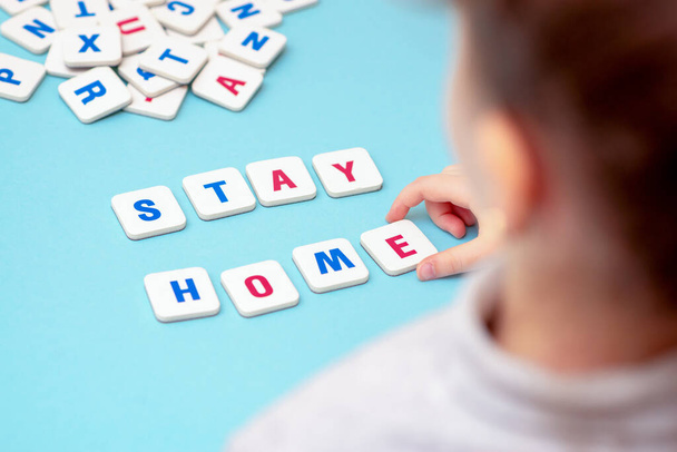 Mano di bambino che fa con lettere parola Stay Home su sfondo blu. Il ragazzo fa massaggi sociali a lettere
. - Foto, immagini
