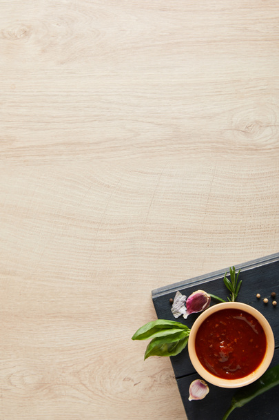 вид на вкусный томатный соус в миске рядом с травами и специями на борту на деревянном столе
 - Фото, изображение