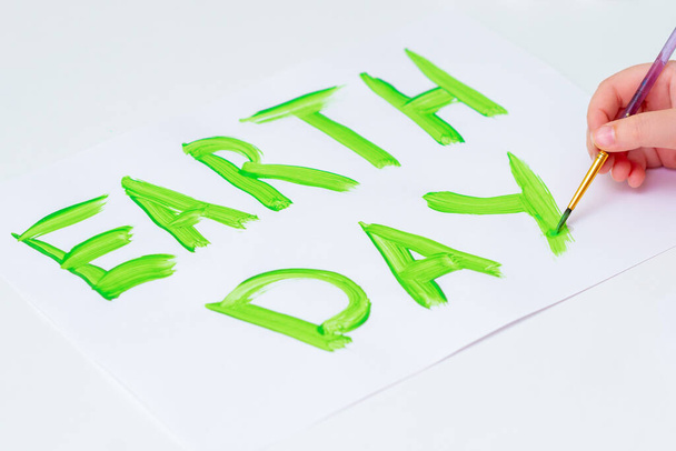 Kinderhände zeichnen Wörter Earth Day mit Pinsel von grünem Aquarell auf weißem Papier. - Foto, Bild