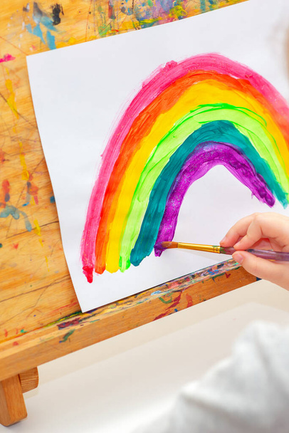 Child is drawing rainbow with watercolors on the sheet of paper on the easel. Creativity concept. - Fotoğraf, Görsel