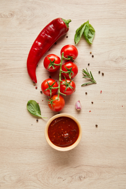 vista superior de delicioso molho de tomate na tigela perto de ingredientes frescos na mesa de madeira
 - Foto, Imagem