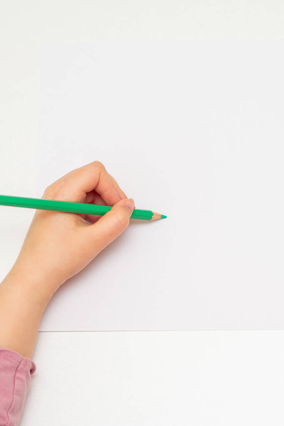 Top view of the child's left hand painting on a white sheet of paper with green pencil. Empty space for your text. Mockup. - Foto, imagen