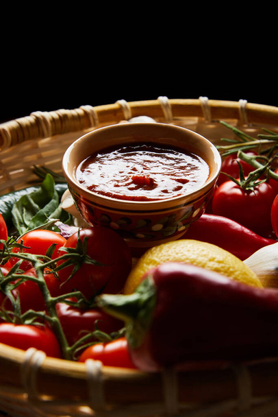 selective focus of delicious tomato sauce with fresh ripe vegetables in basket isolated on black - Photo, Image