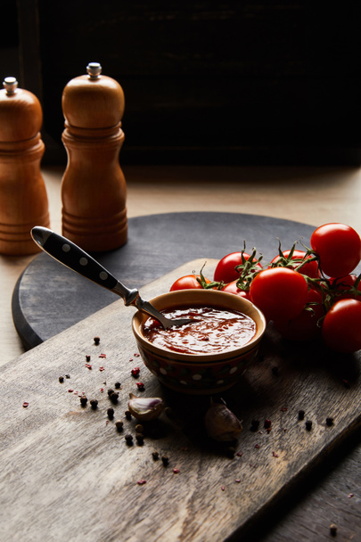 heerlijke tomatensaus in kom met lepel bij tomaten en specerijen op houten bord - Foto, afbeelding