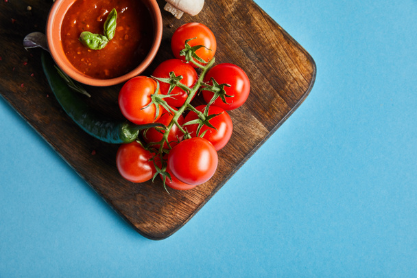 青い背景に新鮮な熟した野菜と木の板の上のボウルにおいしいトマトソースのトップビュー - 写真・画像