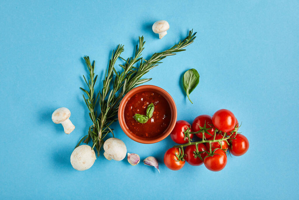 vista superior de la deliciosa salsa de tomate en un tazón cerca de verduras frescas maduras sobre fondo azul
 - Foto, Imagen
