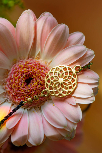 Tiny metal pendant piece in the shape of chakra bracelet on the pink flower  - Photo, Image