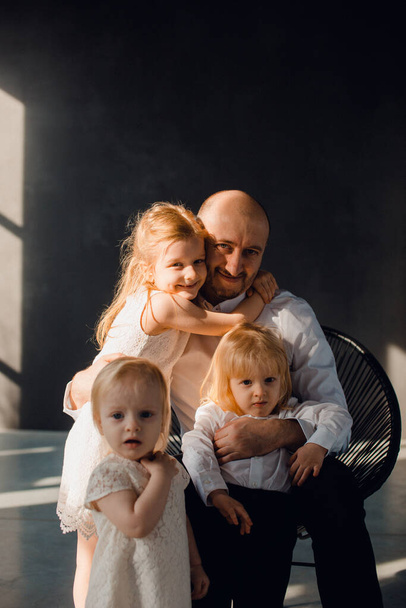 Father and his children in a sunny room with dark walls, children love their father, play with him and hug him - Фото, зображення