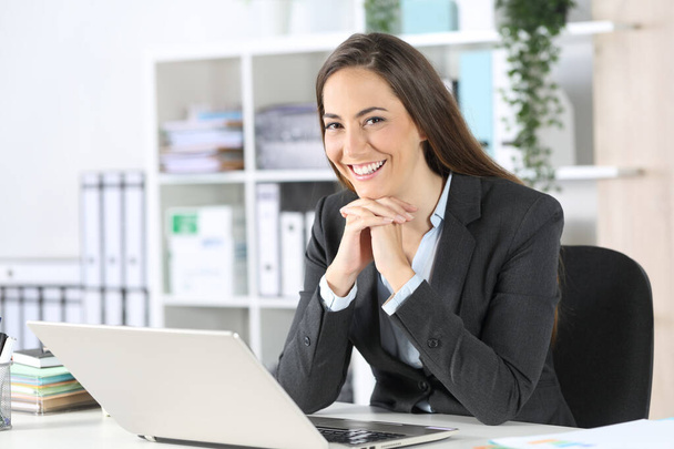 Happy executive woman posing looking at camera sitting on a desk at the office - 写真・画像