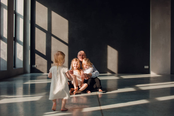 Father and his children in a sunny room with dark walls, children love their father, play with him and hug him - Foto, imagen