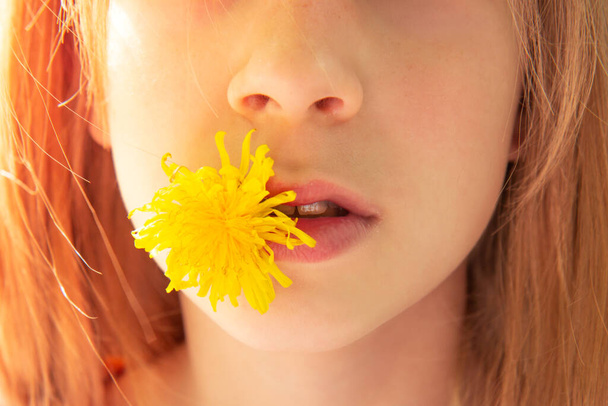 Chica con el pelo rojo sostiene una flor de diente de león en su boca. Cara de cerca. Enfoque selectivo
 - Foto, imagen