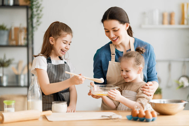 Happy loving family are preparing bakery together. Mother and children daughters girls are cooking cookies and having fun in the kitchen. Homemade food and little helper.  - 写真・画像