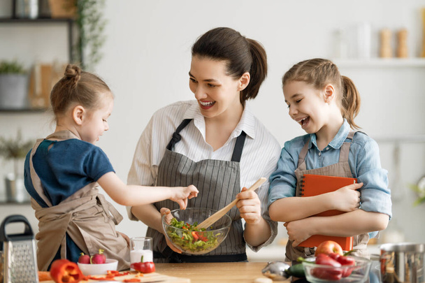 Healthy food at home. Happy family in the kitchen. Mother and children daughters are preparing vegetables. - Foto, Bild