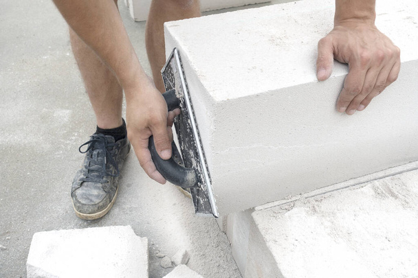 Строитель терки бетонный блок пены (проветривается) перед каменщиком стены
. - Фото, изображение