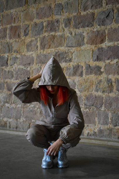 Sportliche Frau mit roten Haaren, die sich auf den Boden lehnt und ein graues Outfit trägt - Foto, Bild