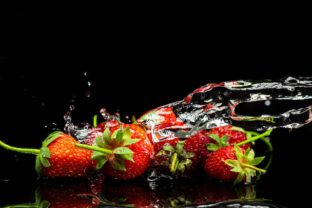 fresh red strawberries isolated on black background in spray and stream of water - Foto, afbeelding