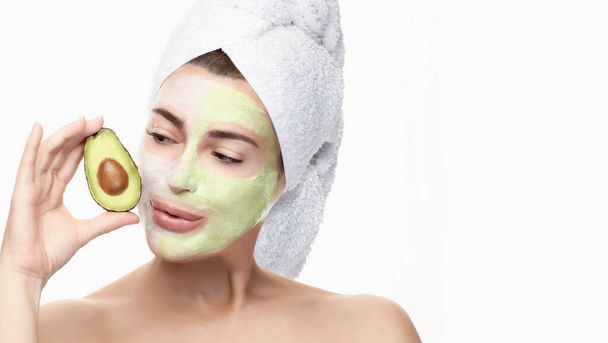 Spa woman with facial beauty mask and half fresh avocado in hand. Beautiful brunette with a towel on head using a facial mask treatment. isolated on white with copy space. Beauty & Skin care concept - Photo, image