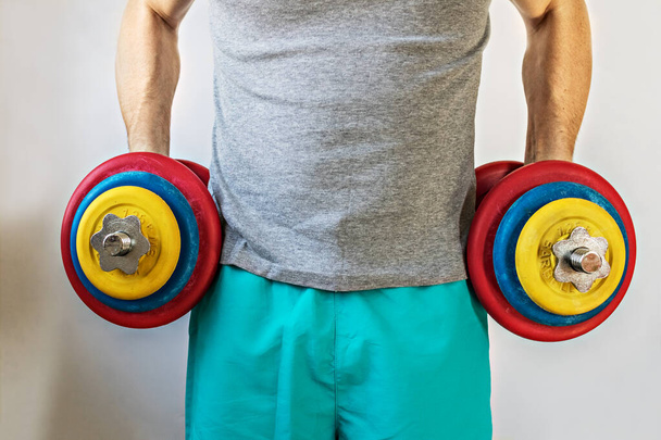 Male athlete holding up heavy dumbbells in two hands. Home Workouts During the Coronavirus Pandemic: A Healthy Lifestyle Concept. - Photo, Image