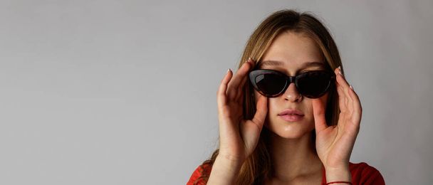 Young attractive woman in red on gray background. Portrait of young woman. Woman posing with sunglasses. Scar on face. - Fotoğraf, Görsel