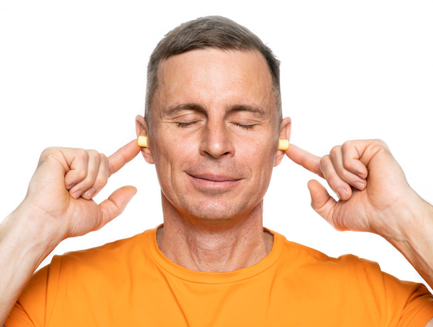 Joven hombre caucásico insertando tapones para los oídos en sus oídos sobre fondo blanco
 - Foto, imagen