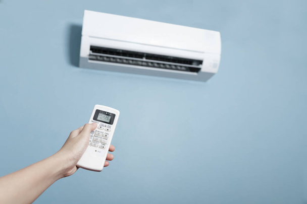 Close-up of men hand operating air conditioner with remote control, Close up shot of hand holding the remote control of white air conditioner on blue color wall. - Photo, Image