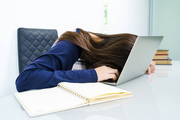 Nuori nainen pitkät hiukset väsynyt opiskelemasta verkossa ja nukahtaa pöydälle kannettavan
 - Valokuva, kuva