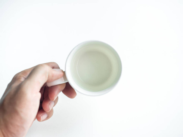 Pusty biały czysty ceramiczny kubek kawy w dłoni izolowane na białym tle, widok z góry. Ręczne trzymanie pustego okrągłego kubka. - Zdjęcie, obraz