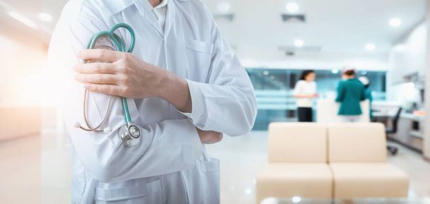 Врач, стоящий со стетоскопом и скрещенными руками, позирует на фоне обследования пациента в палате, вблизи врачей-врачей в клинической больнице. Медицинская страховка
 - Фото, изображение