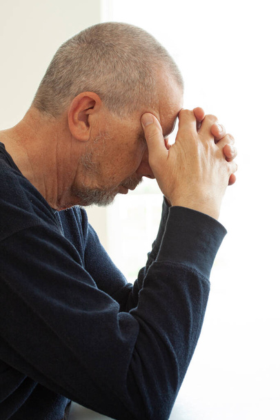 Ongelukkig depressieve man zit aan een tafel gestrest van het werk, angst, gebroken hart en gezondheidszorg concept. Close-up portret. - Foto, afbeelding