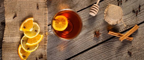 Egy csésze forró tea rusztikus fa deszkán, fahéjas bottal, narancssárgával, citromszeletekkel, mézzel, ánizzsel, szegfűszeggel és egyéb dekorációval. Vintage lapos fekvés. Panoráma - Fotó, kép