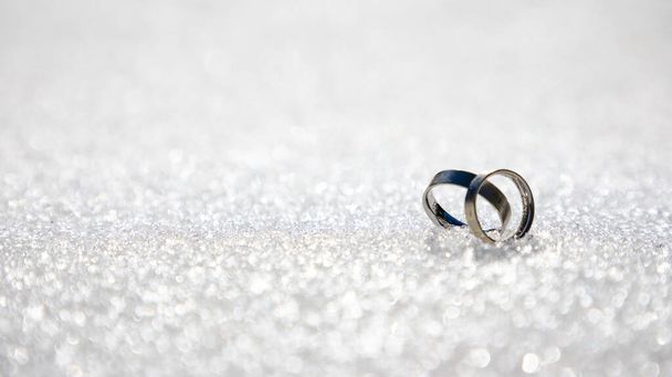 Zilveren of witgouden verlovingsringen op sneeuw- of sprankelende witte achtergrond met kopieerruimte - Foto, afbeelding