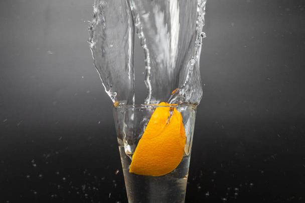 Fatia de laranja caindo e caindo em um vidro espirrando com fundo preto
. - Foto, Imagem