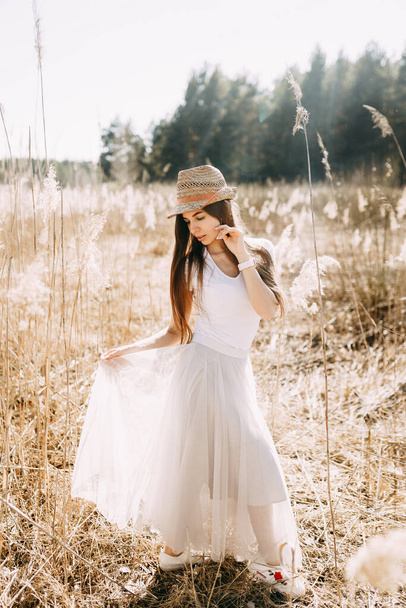 ritratto di una ragazza in un cappello di paglia per strada nell'erba alta secca
. - Foto, immagini