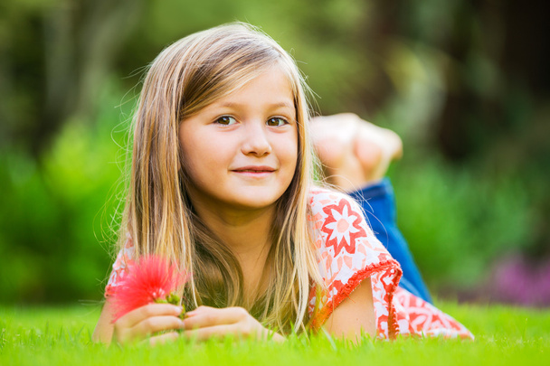 Portrait of a smiling little girl lying on green grass - Fotó, kép