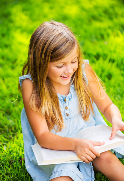 schattig klein meisje het lezen van boek buiten op gras - Foto, afbeelding