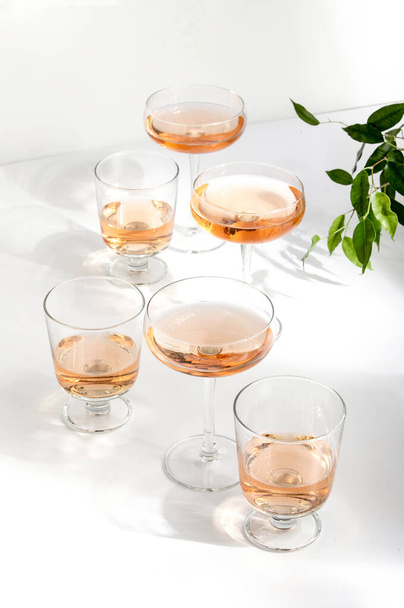 Assortimento di vini rosati, vista frontale di vari bicchieri di vino pieni di vino rosato, in piedi su una superficie del tavolo bianco che riflette i raggi del sole morbidi
 - Foto, immagini