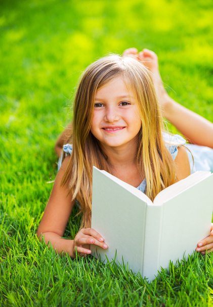 Cute little girl reading book outside on grass - Zdjęcie, obraz